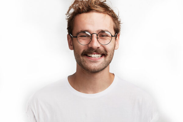 Portrait of cheerful attractive young man with stylish hairdo, pleasant pleased broad smile, dressed casually, has happy expression after realizing positive news, poses against white background.